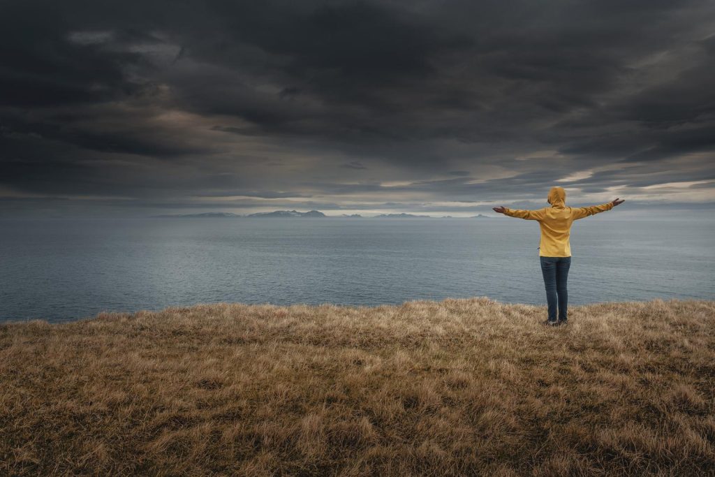Woman on cliff overlooking sea in Iceland in waterproofs