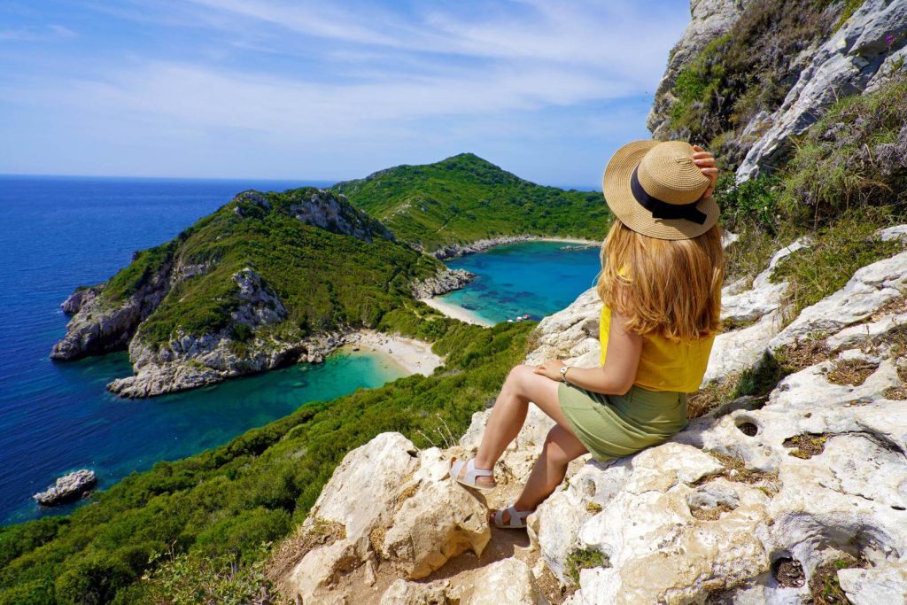 Woman in sandals sitting on rocks overlooking sea in Corfu
