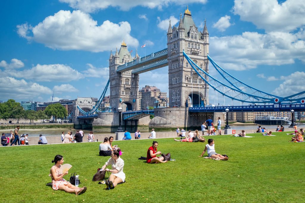 People sitting on lawn in front of Tower Bridge