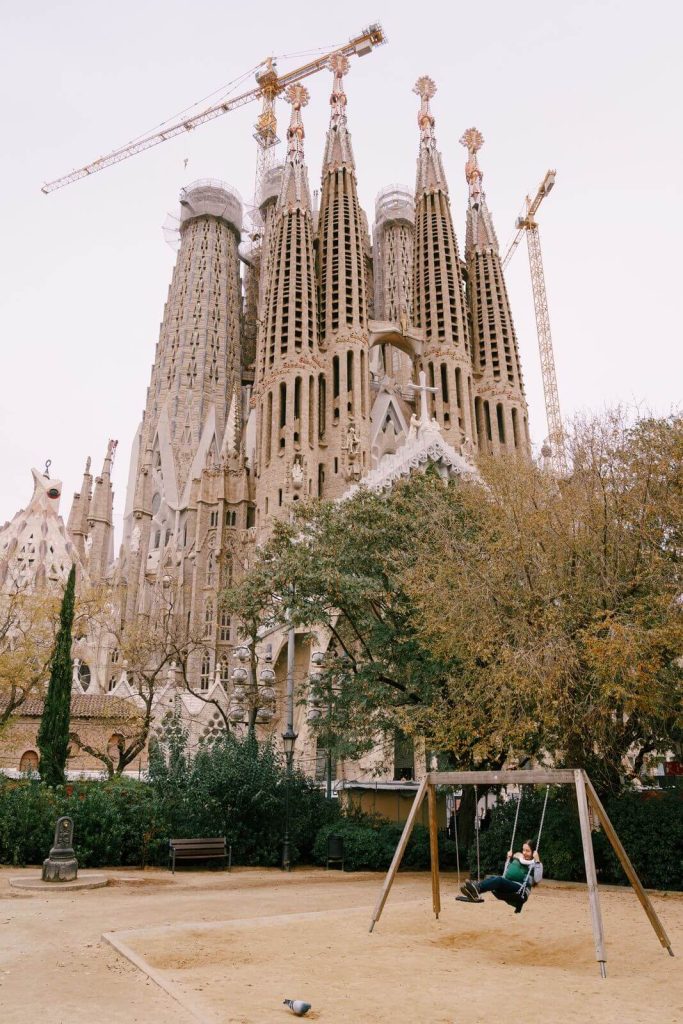 Sagrada Familia in BArcelona in December in background with woman and child on swing in front