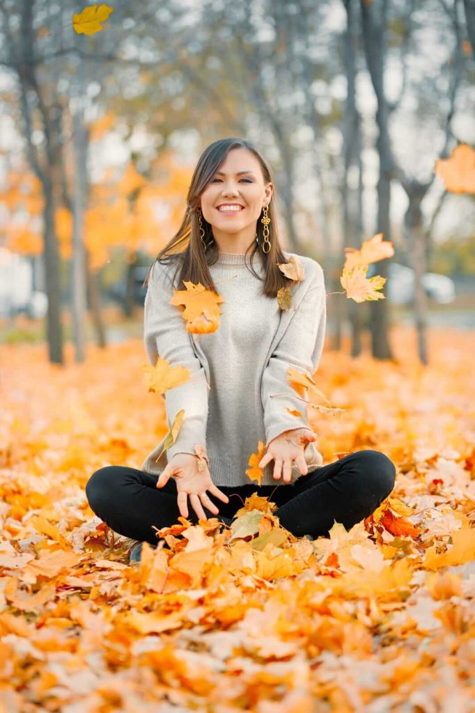 woman in fall clothes sat amongst autmn leaves