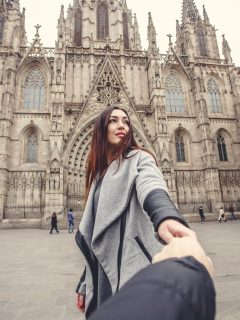 Woman holding man's hand in Winter clothes in front of Barcelona Cathedral