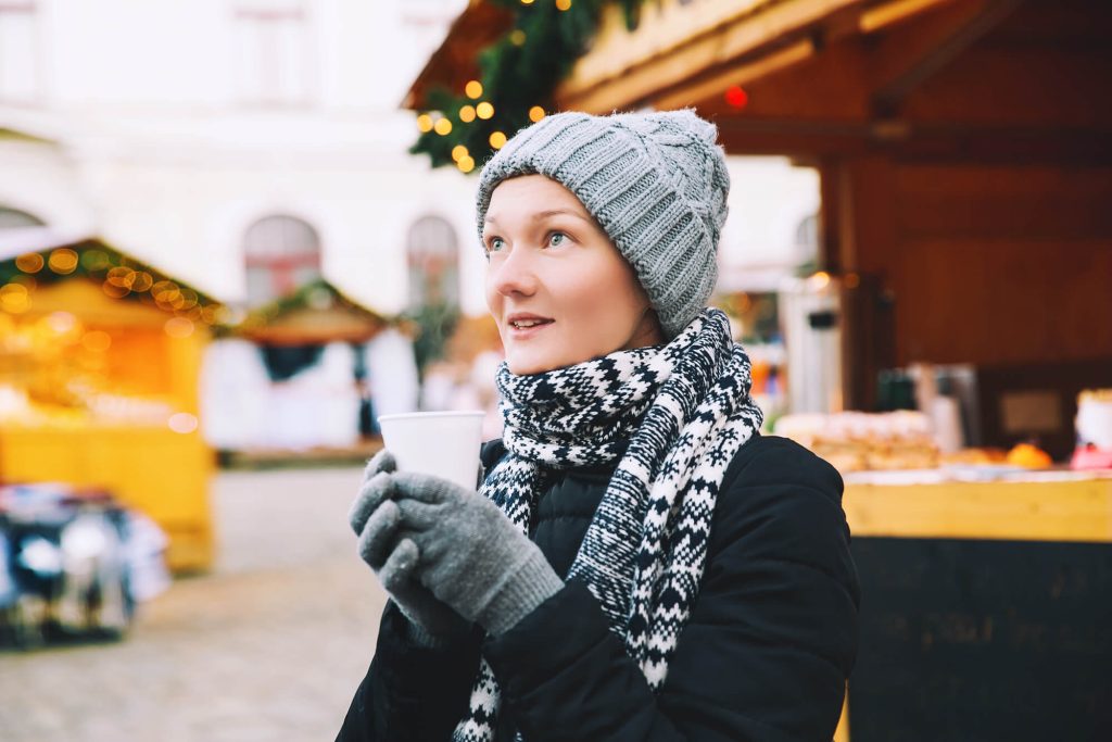 Woman at Christmas Market in Prague in December wearing winter coat and accessories drinking mulled wine