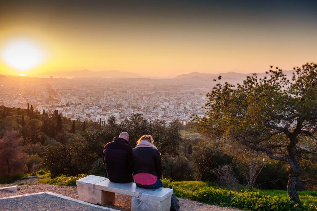 Couple sat in Winter clothes overlooking athens skyline