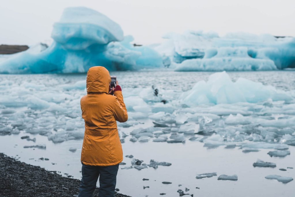 Woman in yellow coat taking pictures of icebergs in Iceland in February