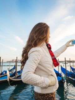 Woman taking photos in Venice in FEbruary wearing a warm coat and gloves