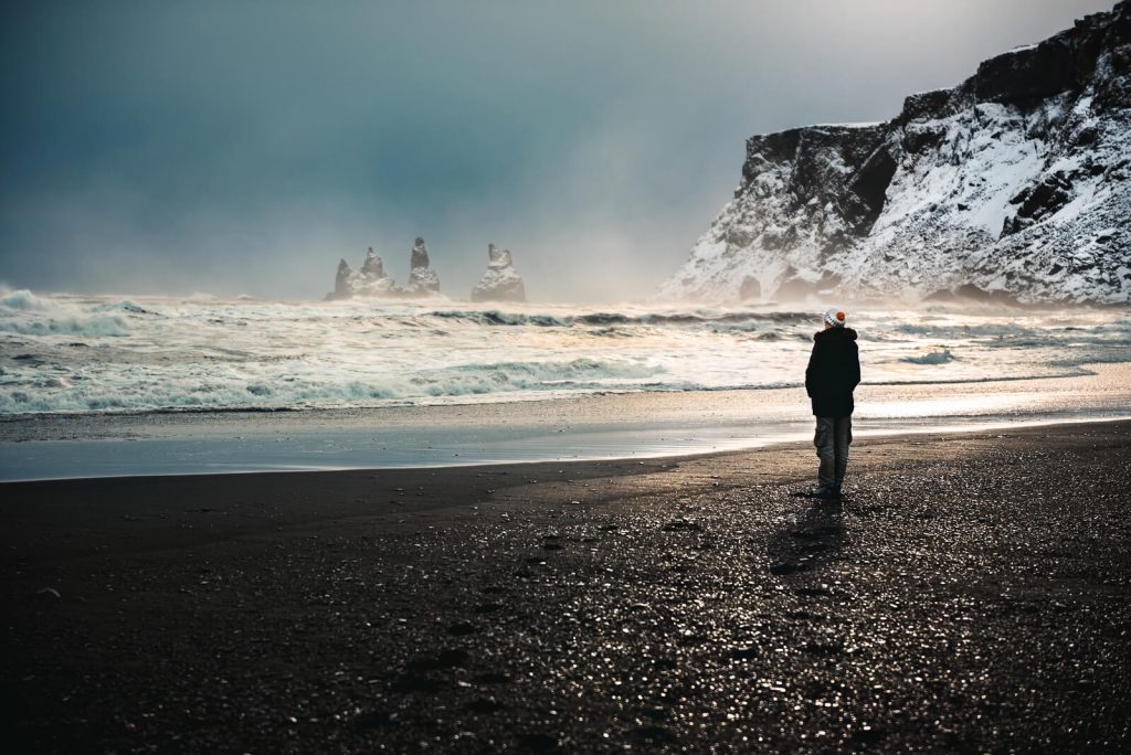 Lone person standing on black sand beach in Iceland in March