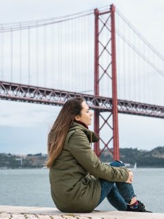 Woman sat with bridge in background in Lisbon in winter