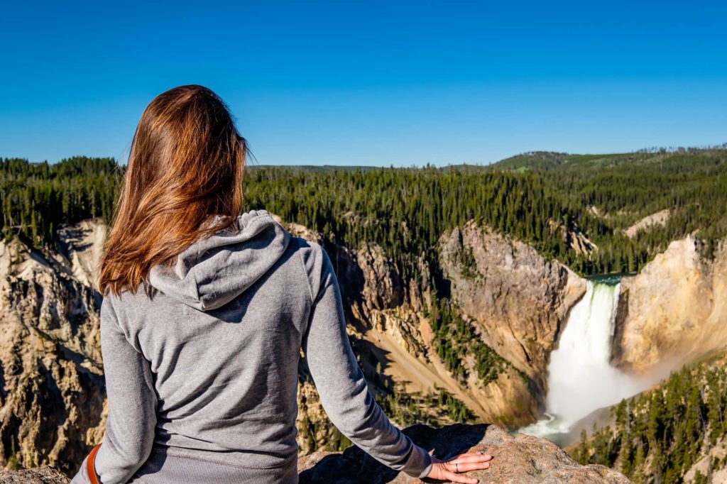 Woman looking at Upper FAlls Waterfall in Yellowstone in Summer with her back to the camea. 