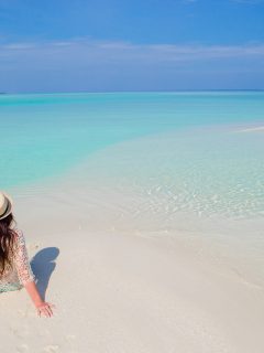 Woman in beach cover and hat sat on the beach in the maldives looking at the sea