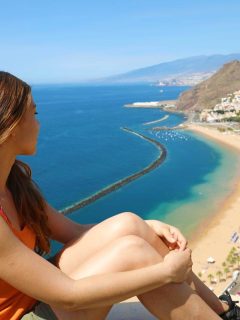 Woman in shorts, tank and bikini high up looking over a beach and sea n Tenerife