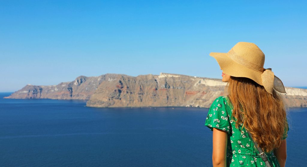 Woman stood with her back to the camera on a cruise ship deck looking at Santorini in the distance