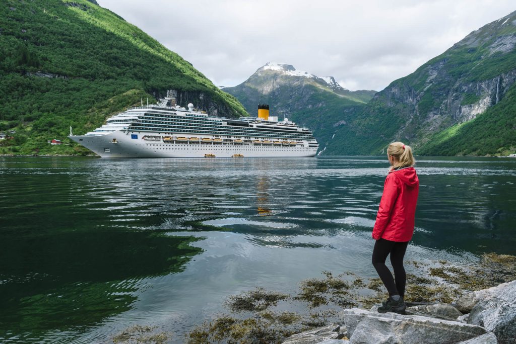 Woman stood by water looking at cruise ship in Norwegian Fjords