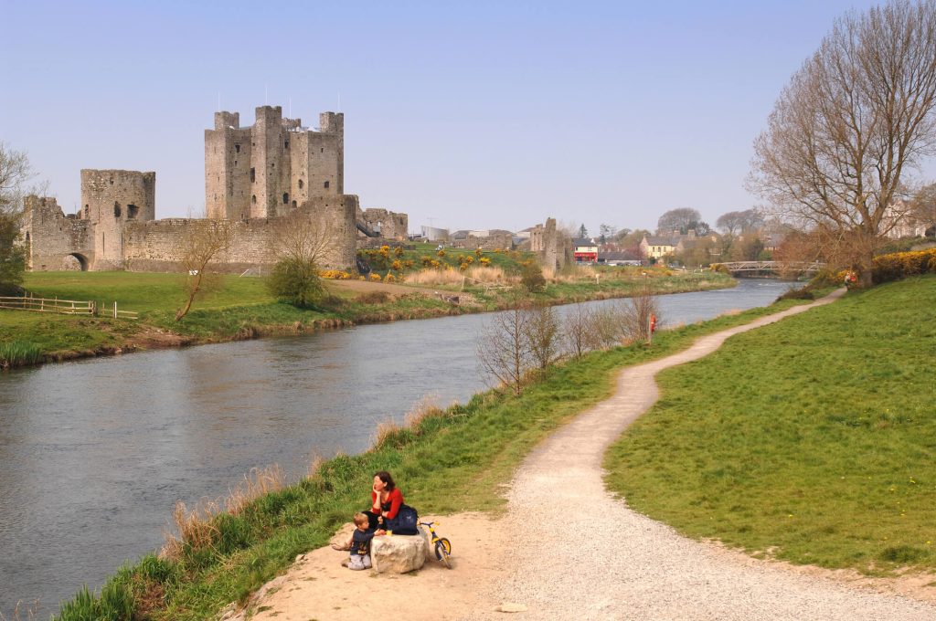 Woman sat on rock next to river looking at castle in Ireland