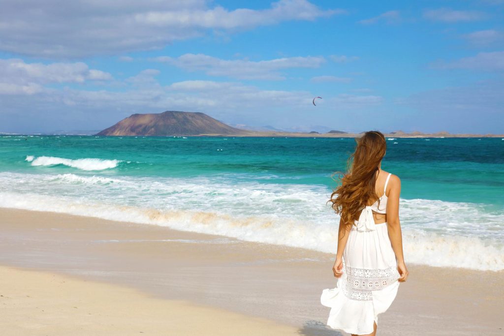 Woman in white dress with back to camera wa on a beach in Fuerteventura